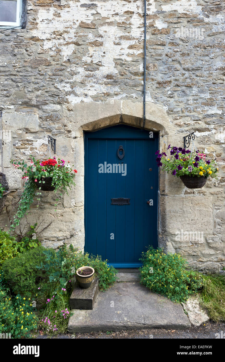 Puerta de madera azul oscuro rodeado con la pared de la casa de piedra  caliza de Cotswold y cestas colgantes de flores Fotografía de stock - Alamy