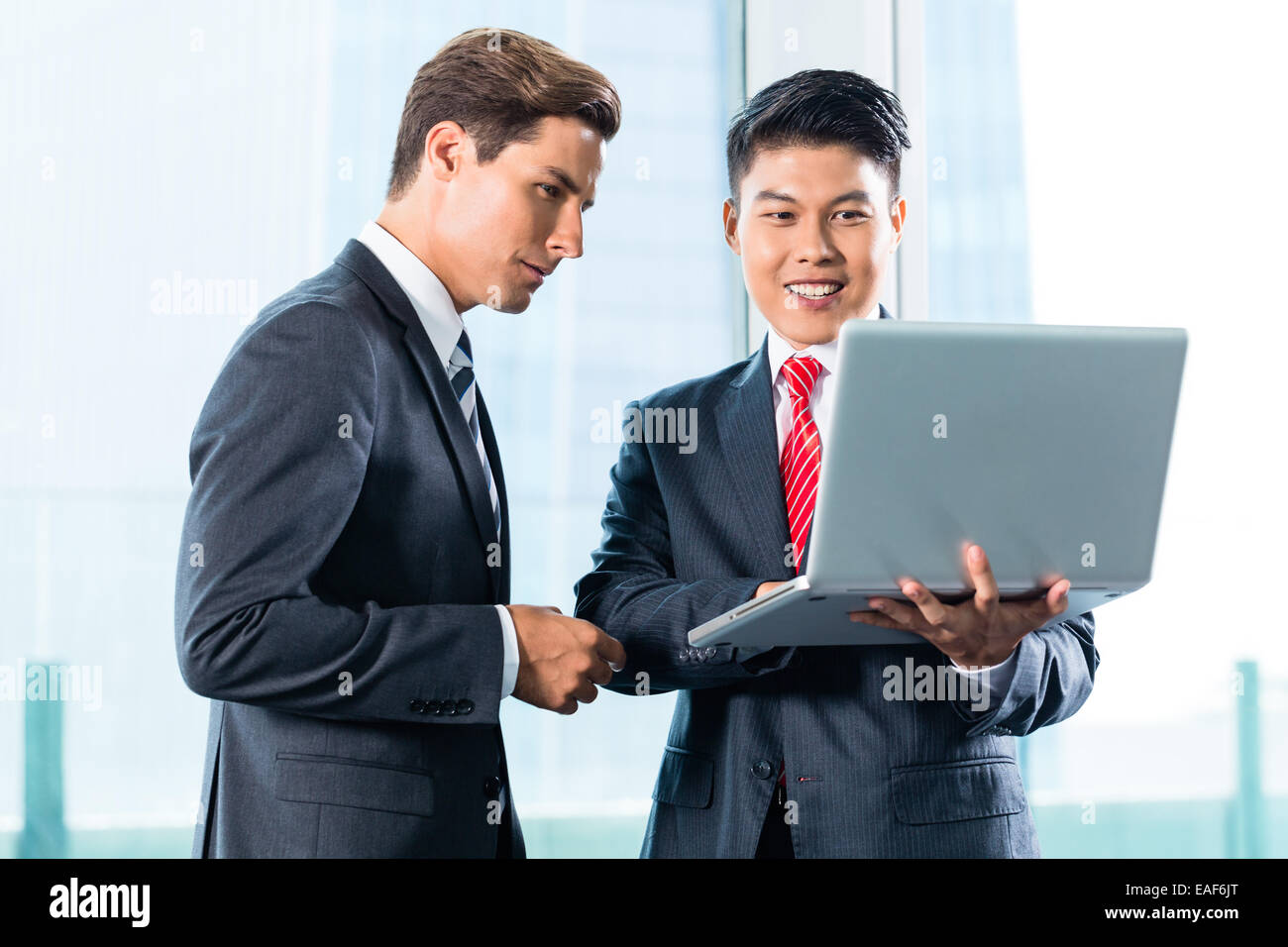 Hombres de negocios asiáticos y caucásicos debatir proyecto sobre portátil Foto de stock