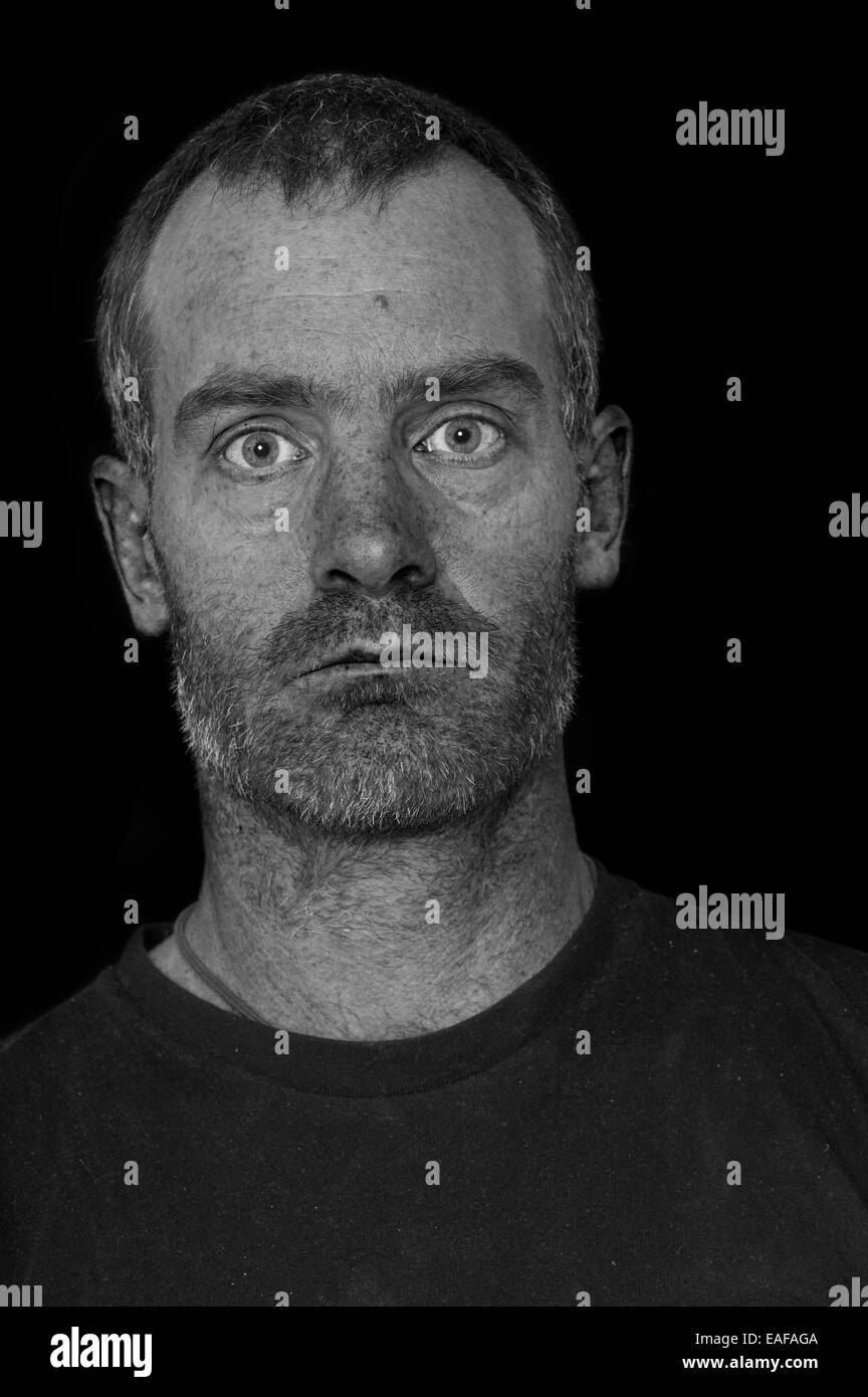 Retrato de un hombre de mediana edad canosa resistente con camiseta negra sobre fondo negro procesado para mostrar la textura de la piel y defectos Foto de stock