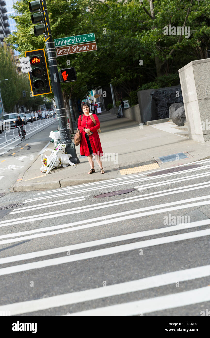 Una mujer en una chaqueta roja / vestido esperando para cruzar la calle Foto de stock