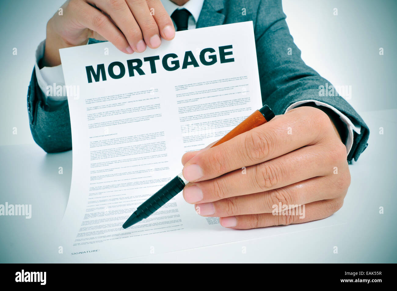 Hombre vestido con un traje sentado en una tabla mostrando un contrato de préstamo hipotecario, y donde el firmante debe firmar Foto de stock