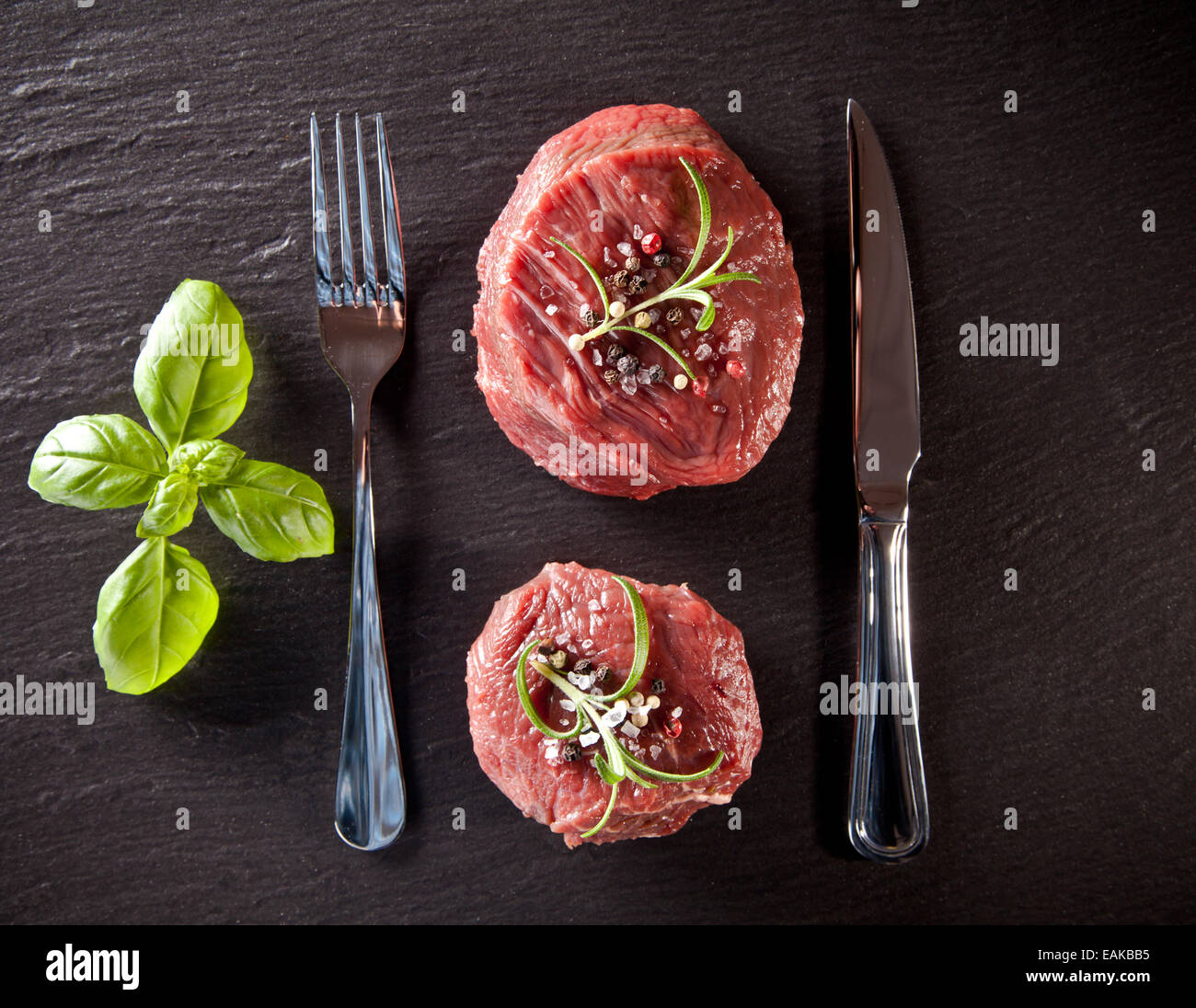 Trozos de carne cruda rojo filetes con hierbas, servido en la piedra negra de la superficie. Disparado desde la vista superior. Foto de stock