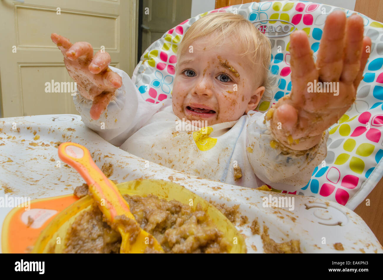 Un niño (ca. 18 meses de edad) hace una terrible lío de su comida. Foto de stock