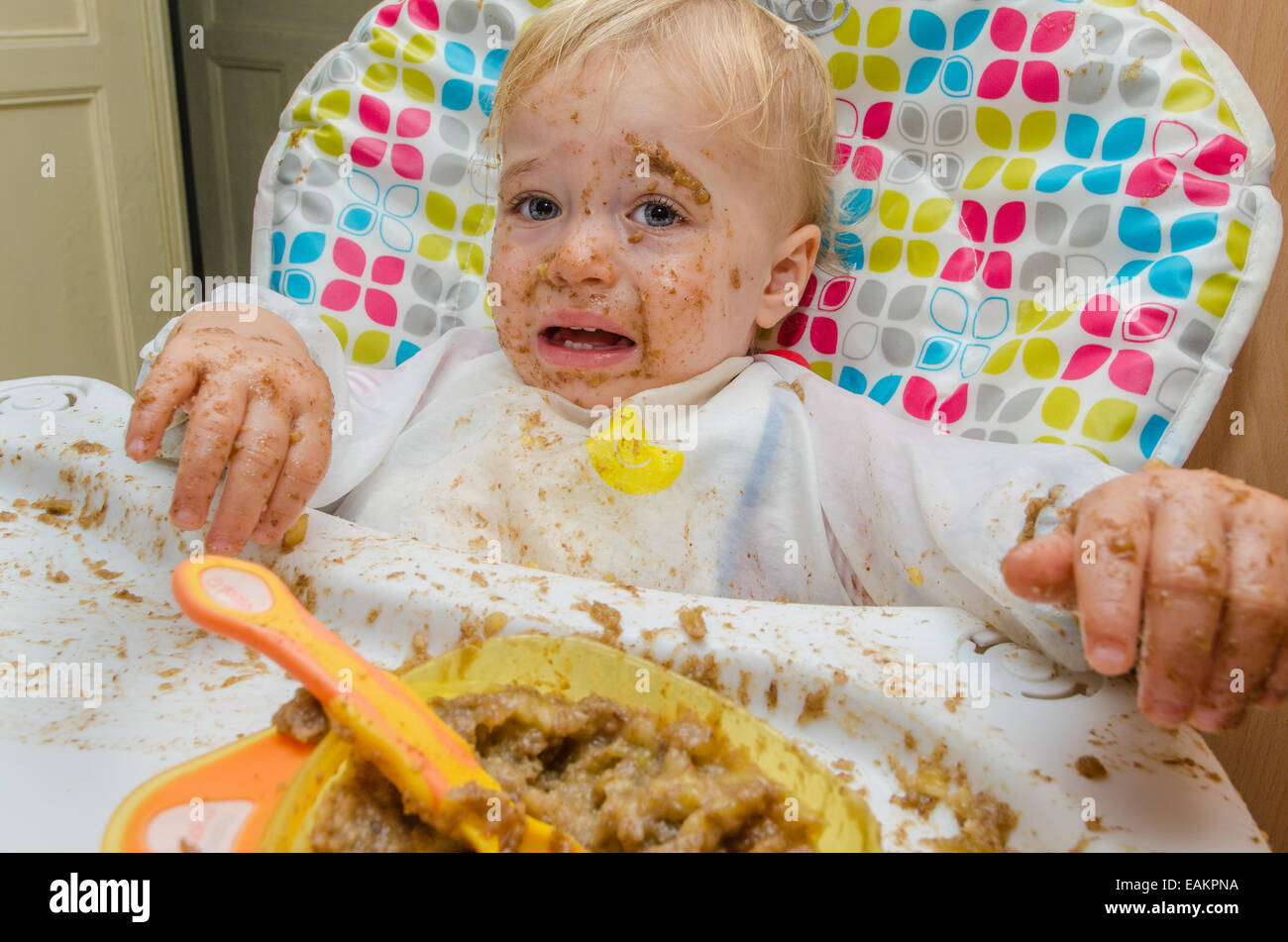 Un niño (ca. 18 meses de edad) hace una terrible lío de su comida. Foto de stock