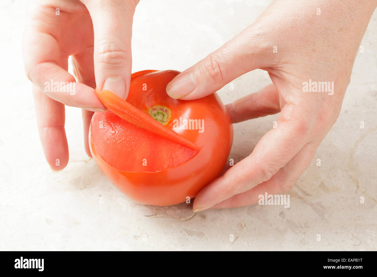 Manos quitando la piel de un tomate Foto de stock