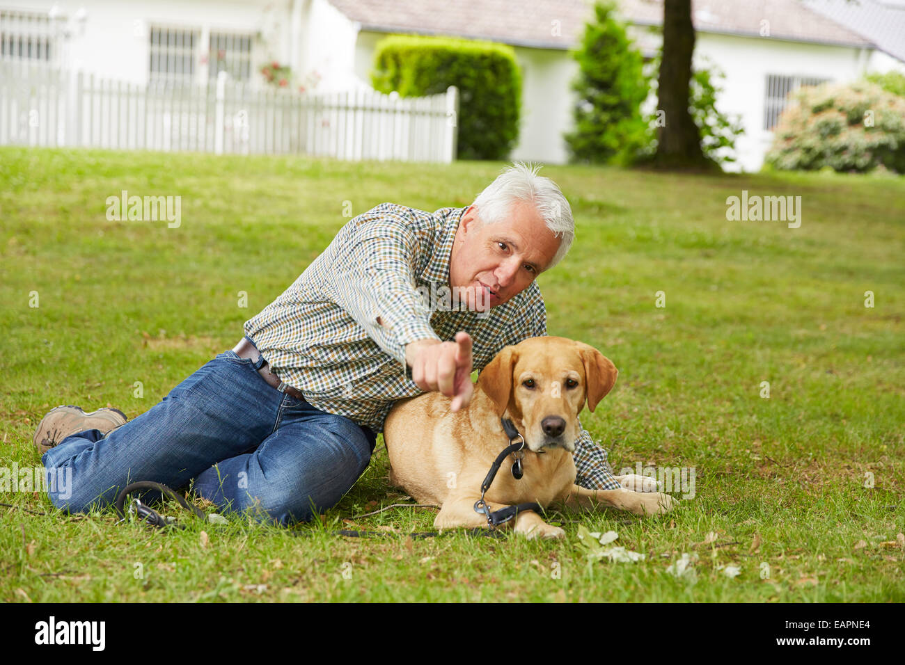 Hombre sentado con perro senior en el jardín de enfrente de la casa Foto de stock