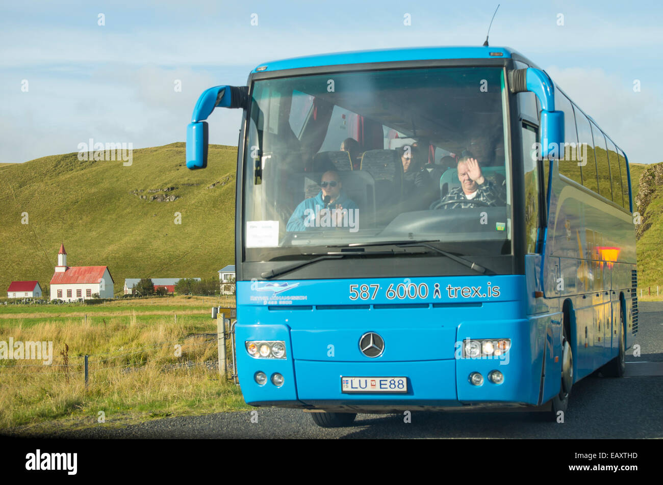En autocar con conductor y guía de grupo de tour conduce en una carretera cerca de una zona agrícola rural en la carretera de circunvalación, Islandia Foto de stock