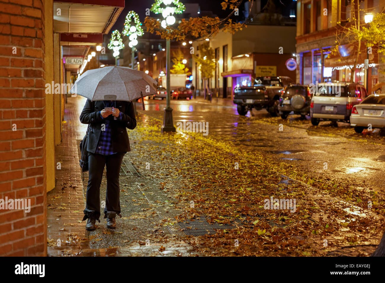 La mujer móvil con sombrilla en el centro de calle en la noche lluviosa de Victoria, British Columbia, Canadá. Foto de stock