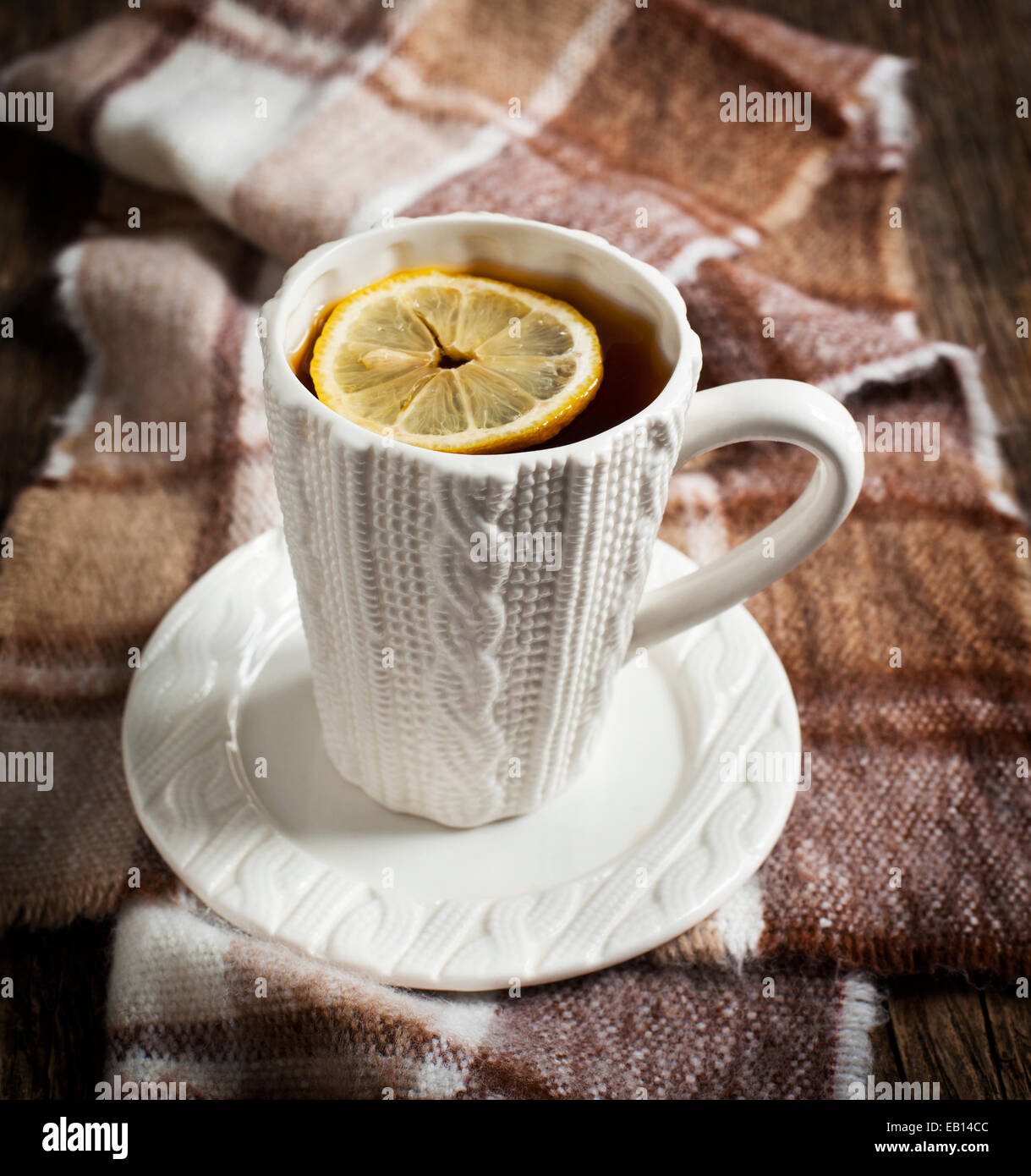 Taza de té caliente con limón y pañuelo sobre mesa de madera. Foto de stock