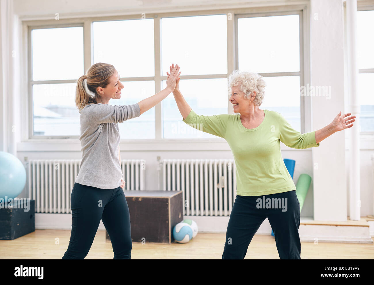 Mujer Senior High Five dando a su fisioterapeuta en rehab. Feliz anciana celebrando el éxito con su fitness instr Foto de stock