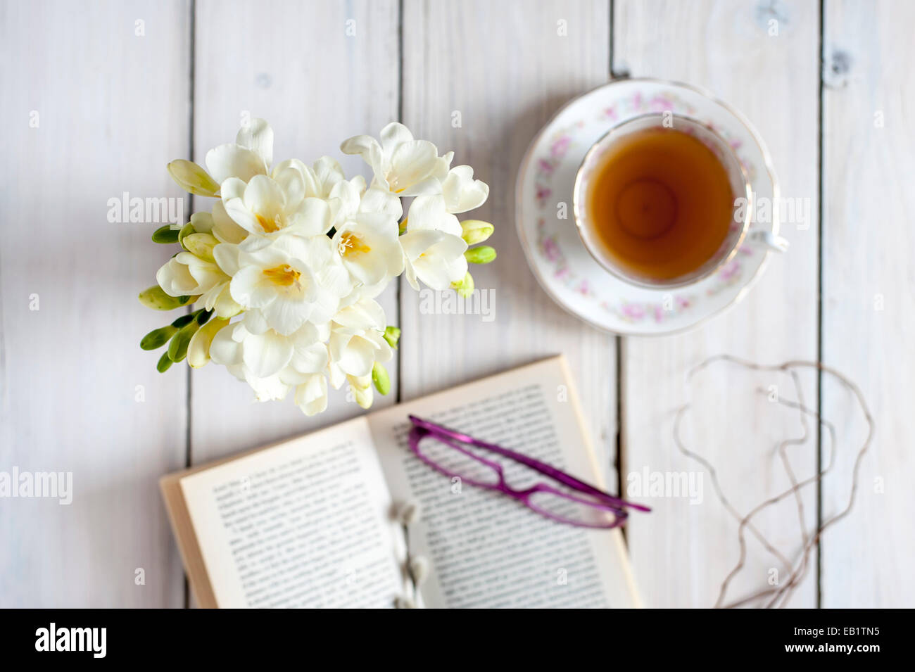 La hora del té - té servido en vaso vintage con posy de fresias, libro blanco y gafas Foto de stock