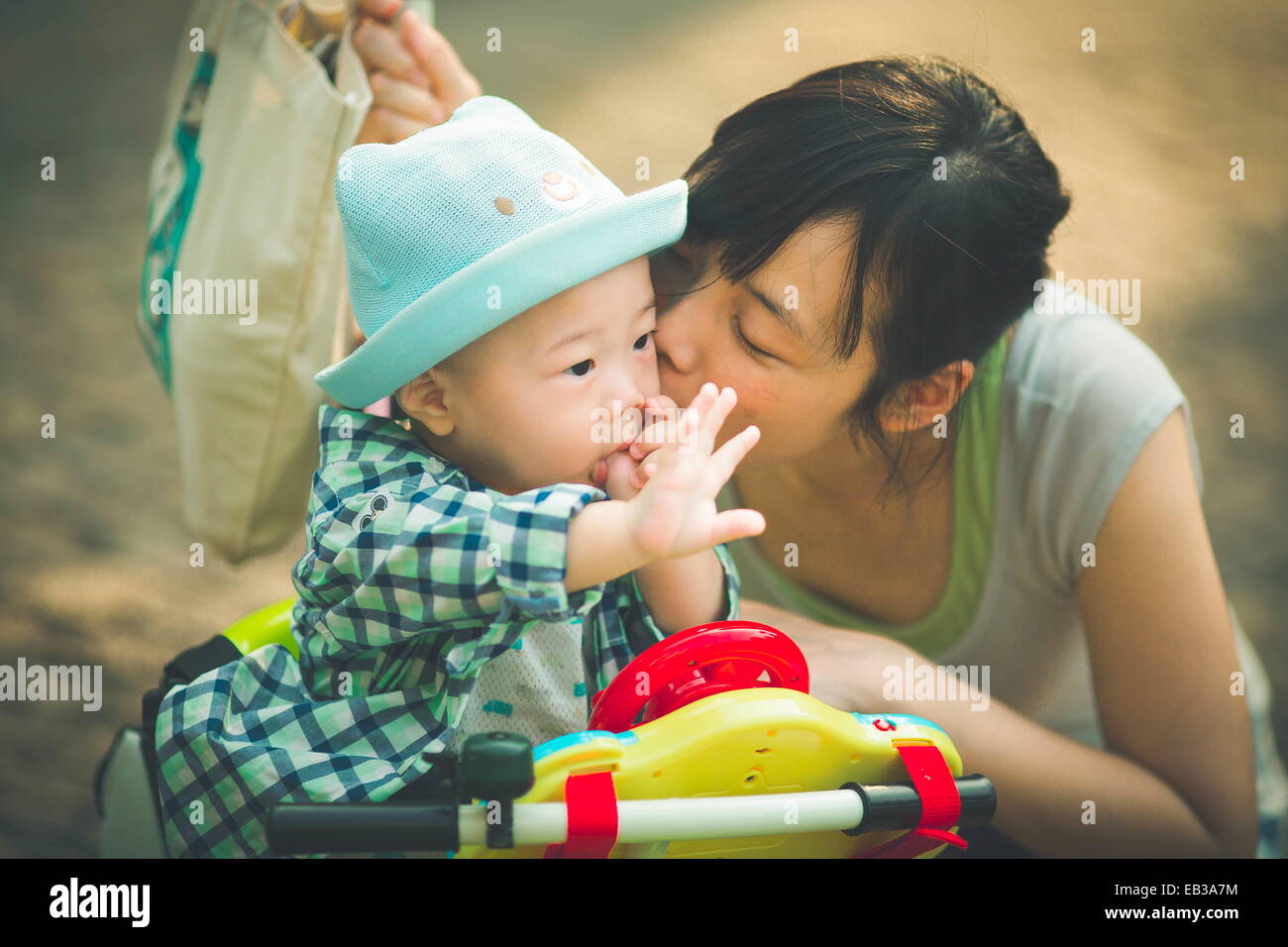 Madre besando a su hijo mientras estaba en su triciclo de juguetes Foto de stock