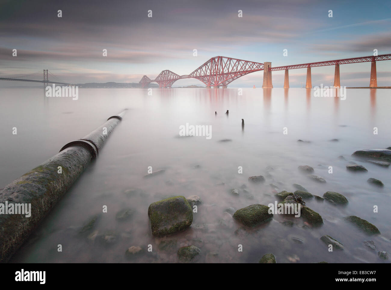Reino Unido, Escocia, Queensferry, puente ferroviario de Forth vistos desde el otro lado de un mar tranquilo, con una tubería submarina ejecutándose en primer plano Foto de stock
