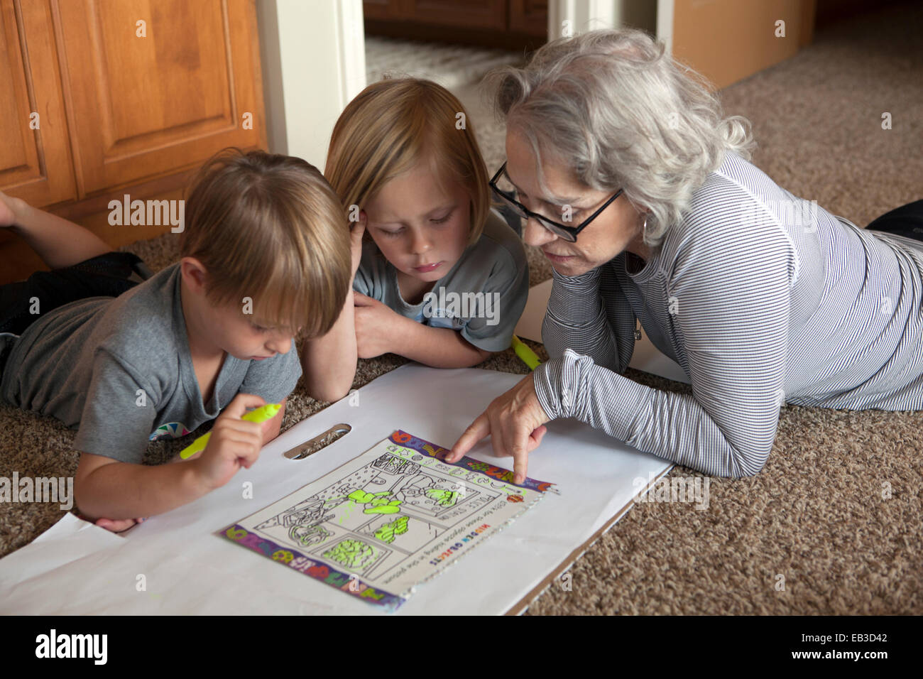 Abuela caucásica y nietos coloreando juntos en el piso Foto de stock