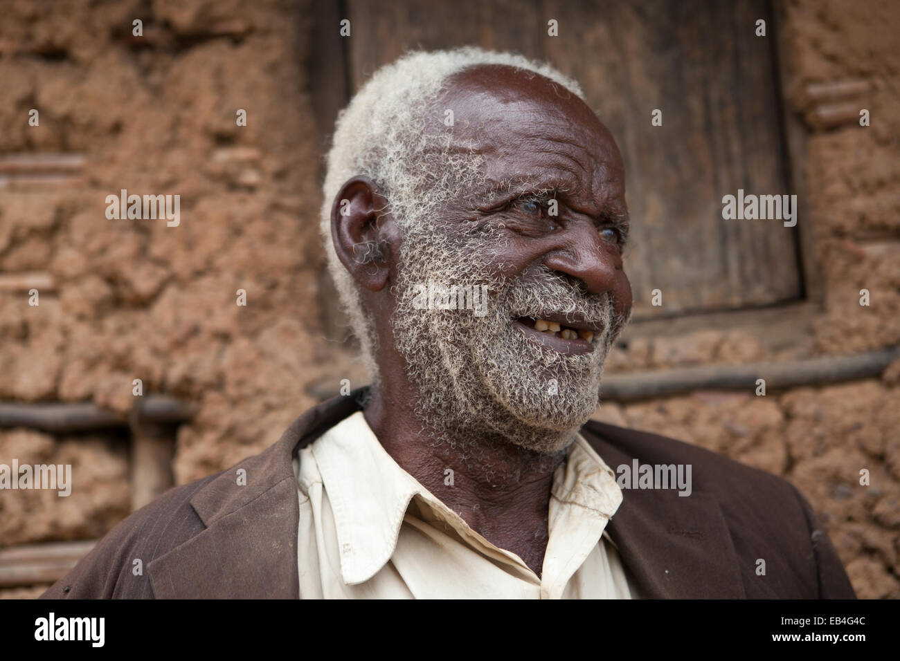 Un anciano se sienta junto a una casa hecha de tierra y madera. Foto de stock