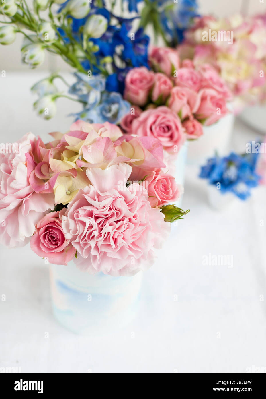 Delphinium azul, rosa rosas, hortensias, clavel en latas decoradas con papel de acuarela pintada de blanco - telón de fondo Foto de stock