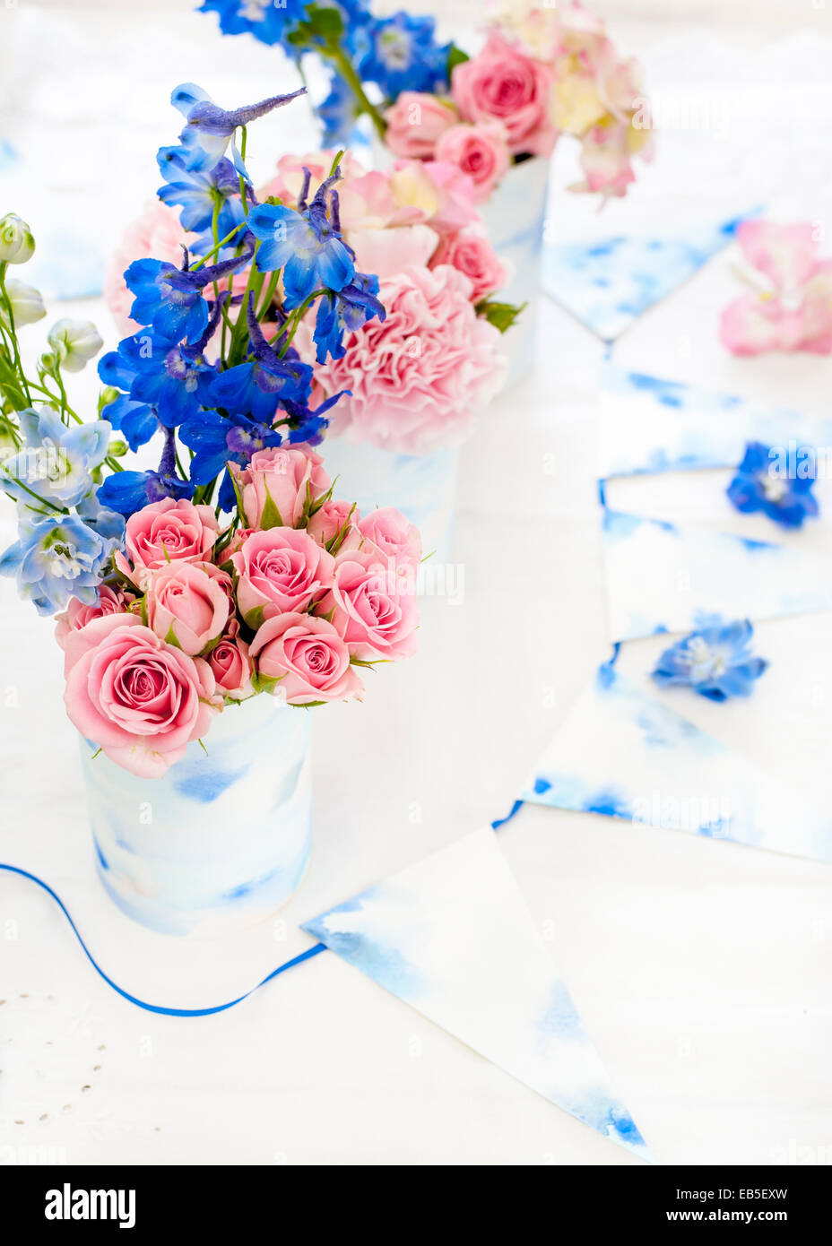 Delphinium azul, rosa rosas, hortensias, clavel en latas decoradas con papel de acuarela pintada de color blanco y azul y bunting Foto de stock
