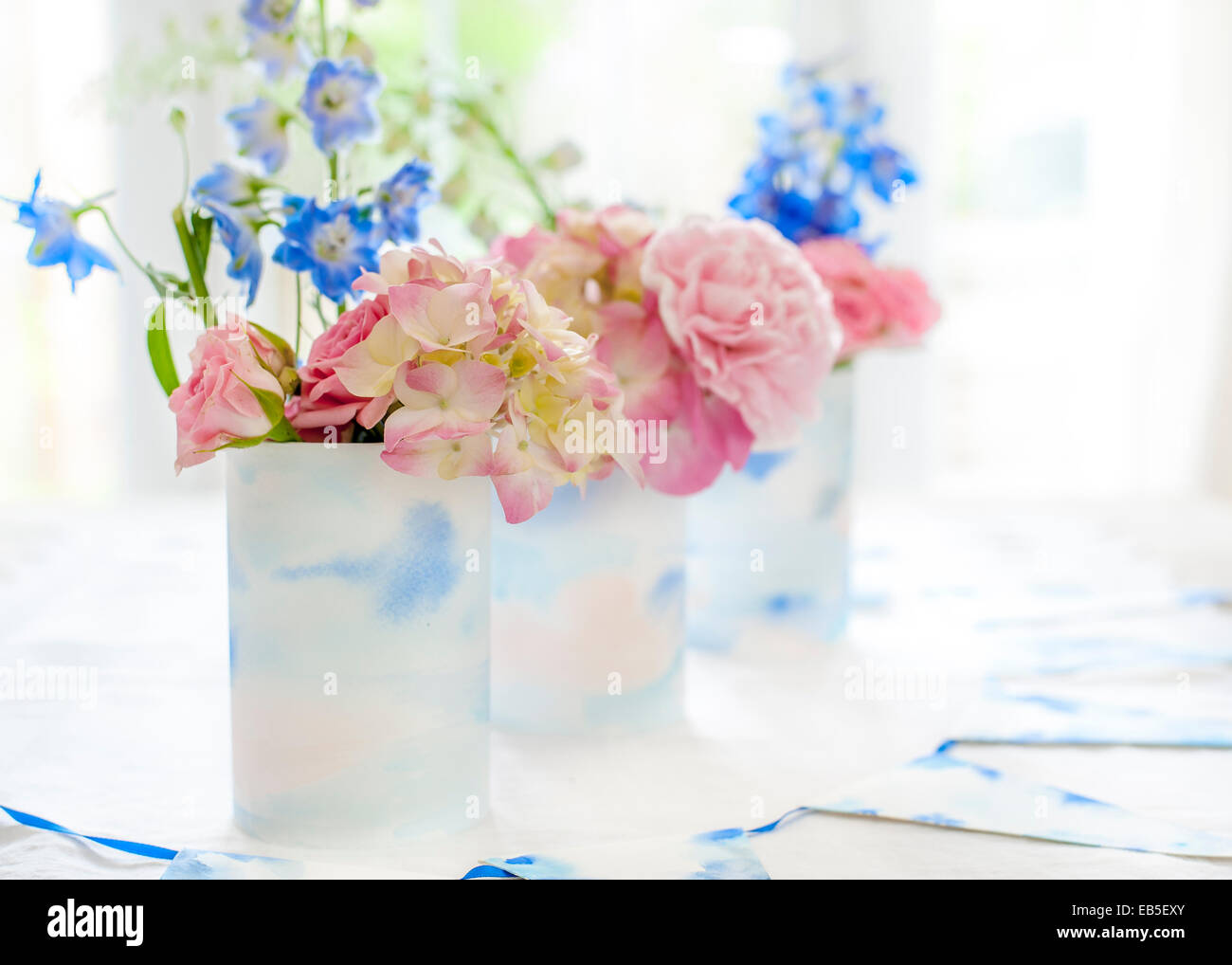Delphinium azul, rosa rosas, hortensias, clavel en latas decoradas con papel de acuarela pintada de color blanco y azul y bunting Foto de stock