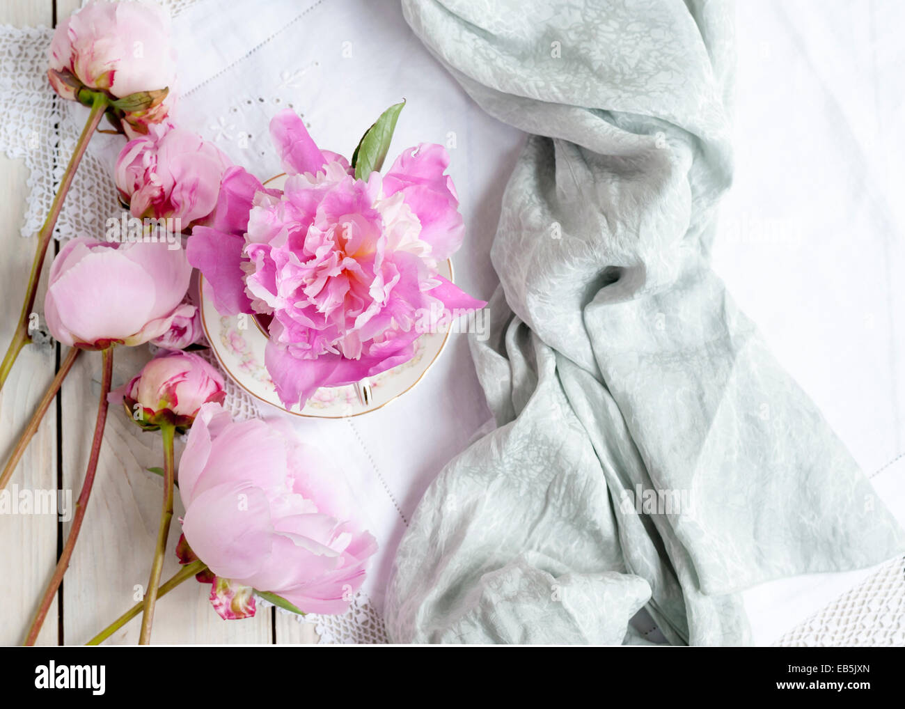 Una creativa de corte rosa Sarah Bernhardt peonías sobre la mesa, una flor en un vaso de agua vintage en tela de encaje blanco Foto de stock