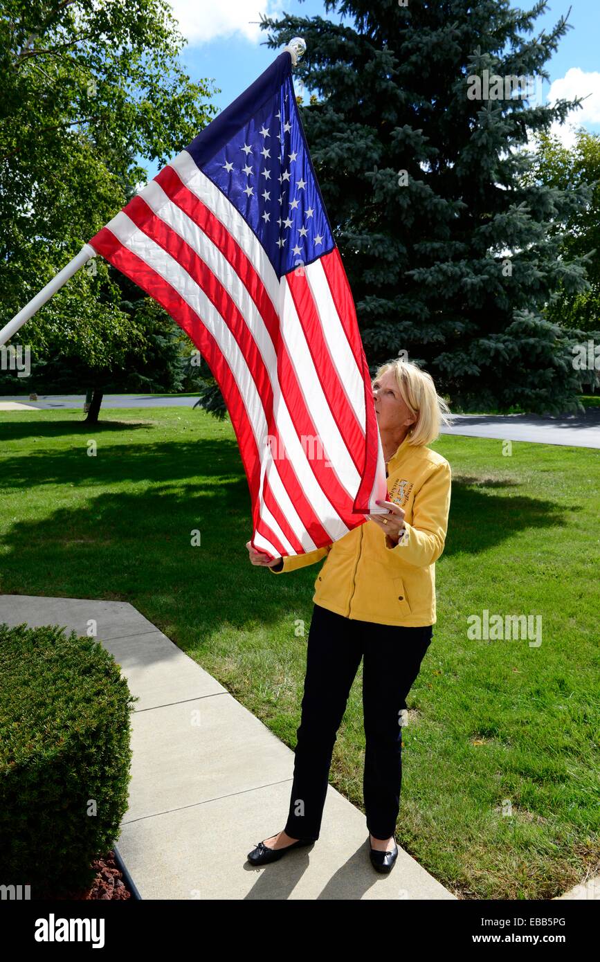 Mujer endereza la bandera en el mástil en la parte delantera de la casa Foto de stock