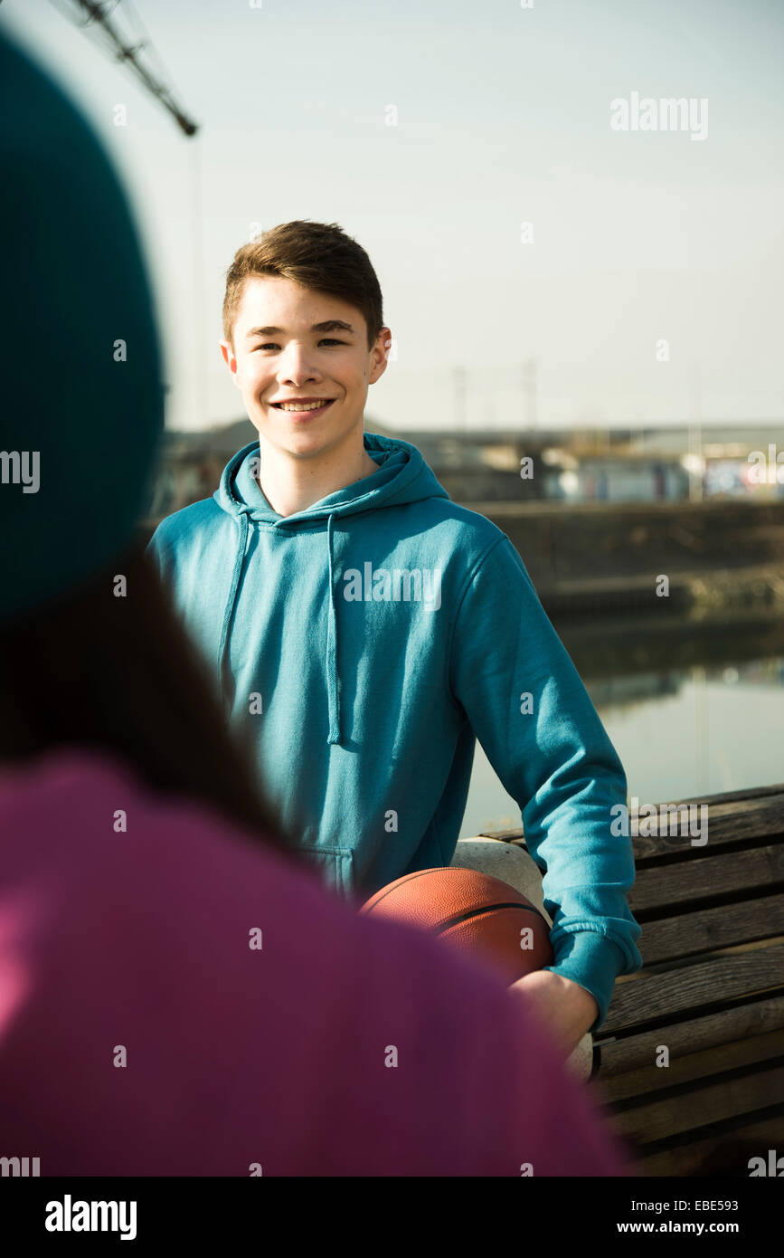 Teeange niño sosteniendo el baloncesto al aire libre, sonriente y mirando al adolescente, área industrail, Mannheim, Alemania Foto de stock