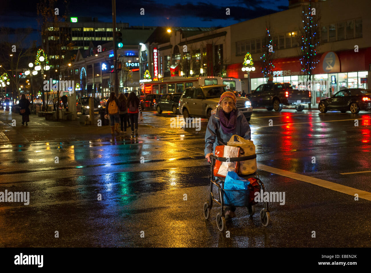 Anciana con walker caminar en el centro de Victoria, en la noche lluviosa de Victoria, British Columbia, Canadá. Foto de stock