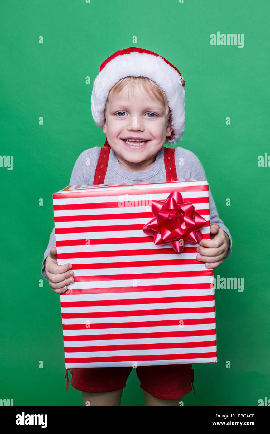 Poco sonriente niño sosteniendo el cuadro actual. Concepto de Navidad. Retrato de estudio sobre fondo verde Foto de stock