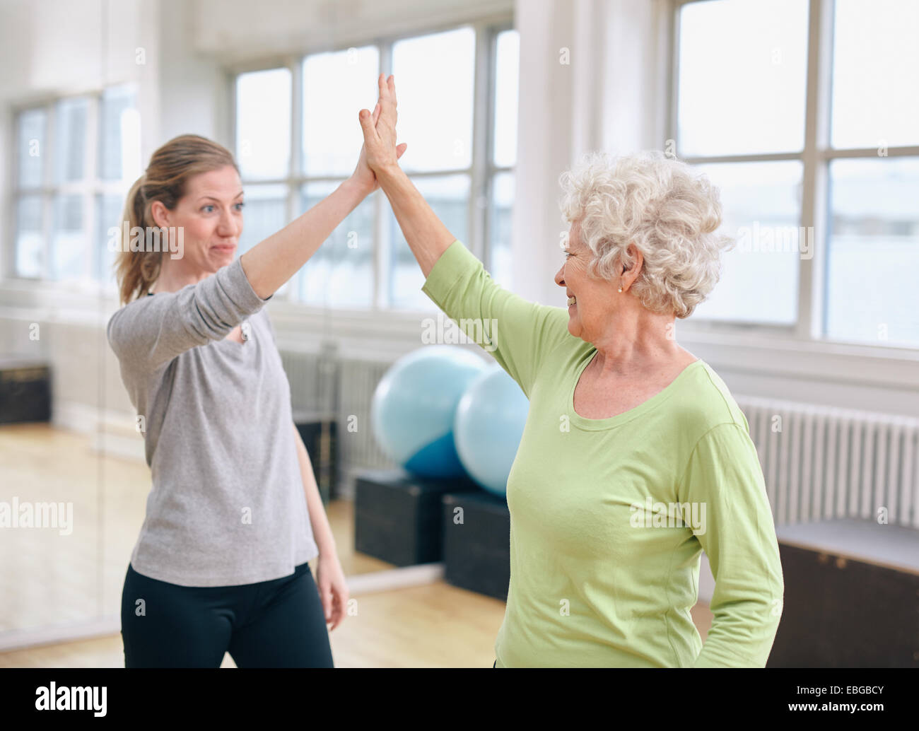 Mujer Senior High Five dando a su entrenador personal en un gimnasio. Emocionada anciana regocijo salud éxito con su instructor en Foto de stock