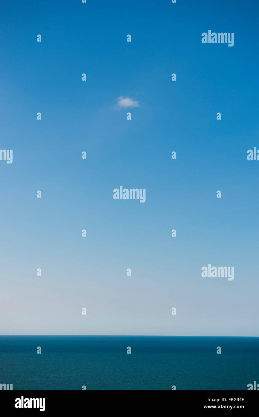 Una pequeña nube blanca en un cielo azul sin nubes contrario a través de un océano de agua de mar Foto de stock