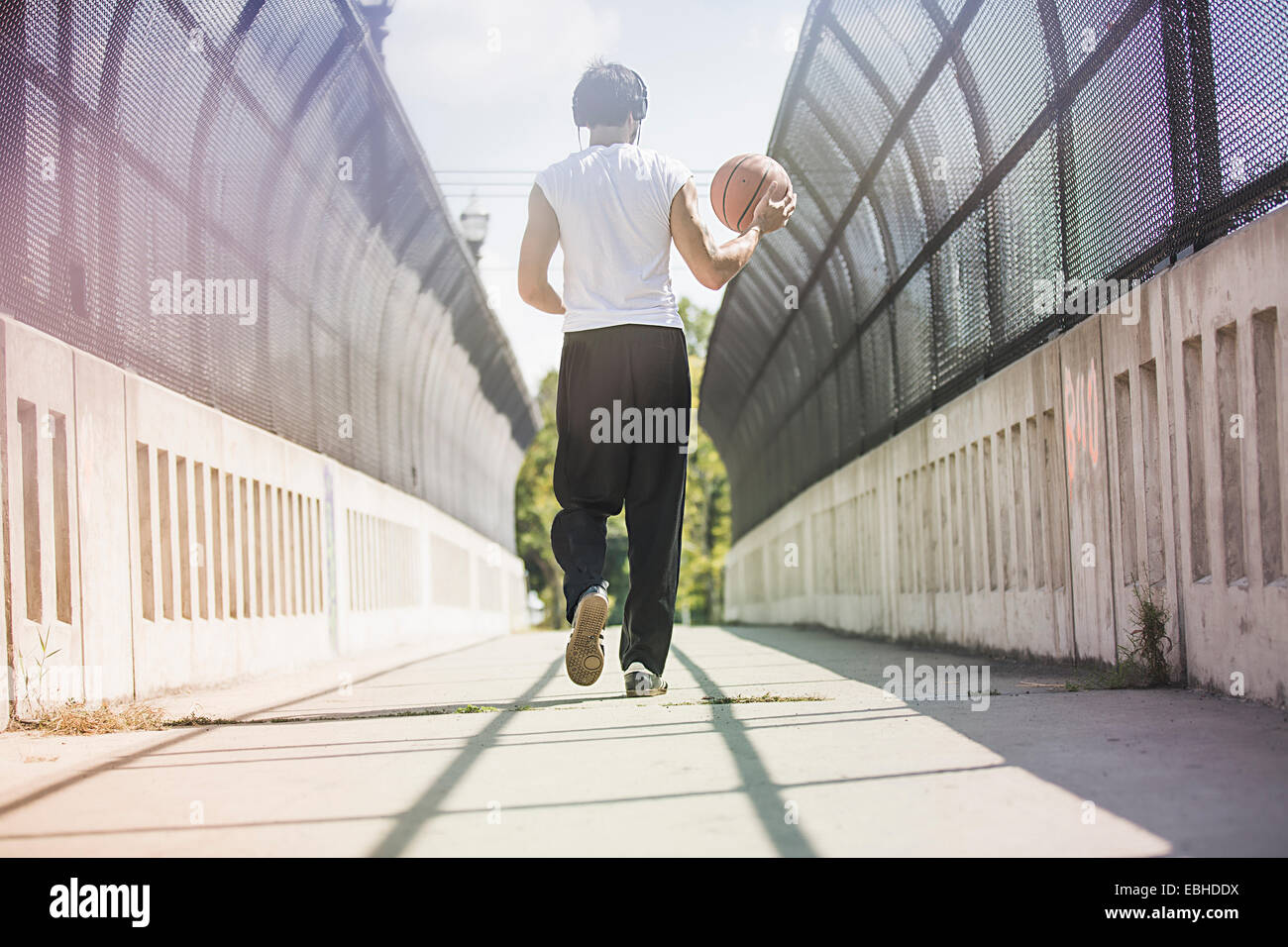 Vista trasera del joven jugador de baloncesto masculino caminando a lo largo de la pasarela llevando la bola Foto de stock