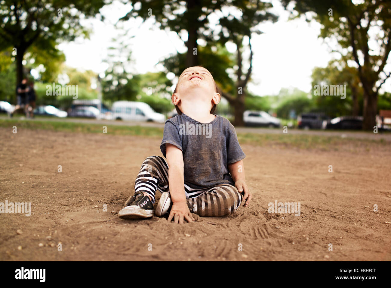 Niño varón sentado en el parque mirando hacia arriba Foto de stock