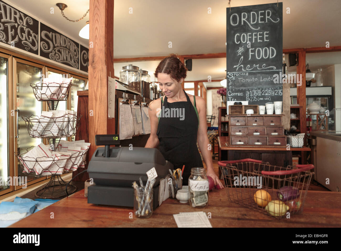 Asistente de ventas femenino mediante la casilla de salida hasta en Country Store cafe Foto de stock