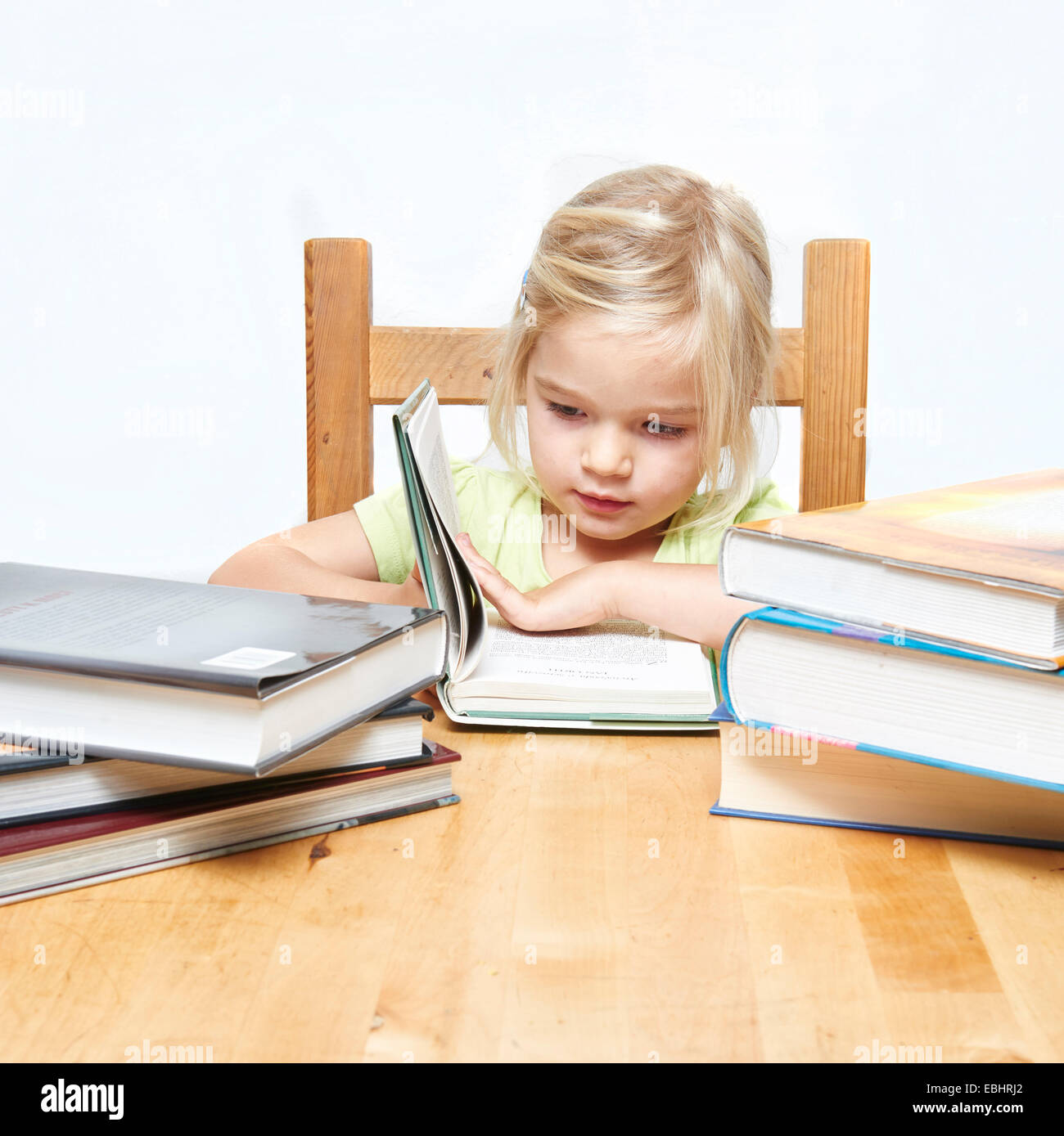 Lindo niño joven rubia chica leyendo y estudiando su libro, fondo blanco, pila de libros Foto de stock