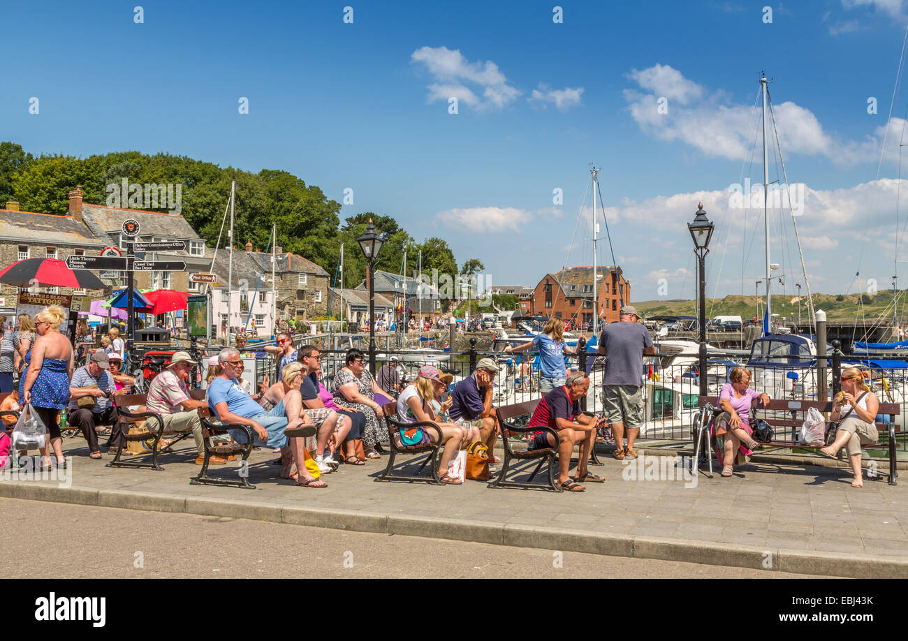 Turistas sentados en bancos disfrutando del sol de verano en Padstow Cornwall Inglaterra Reino Unido Foto de stock