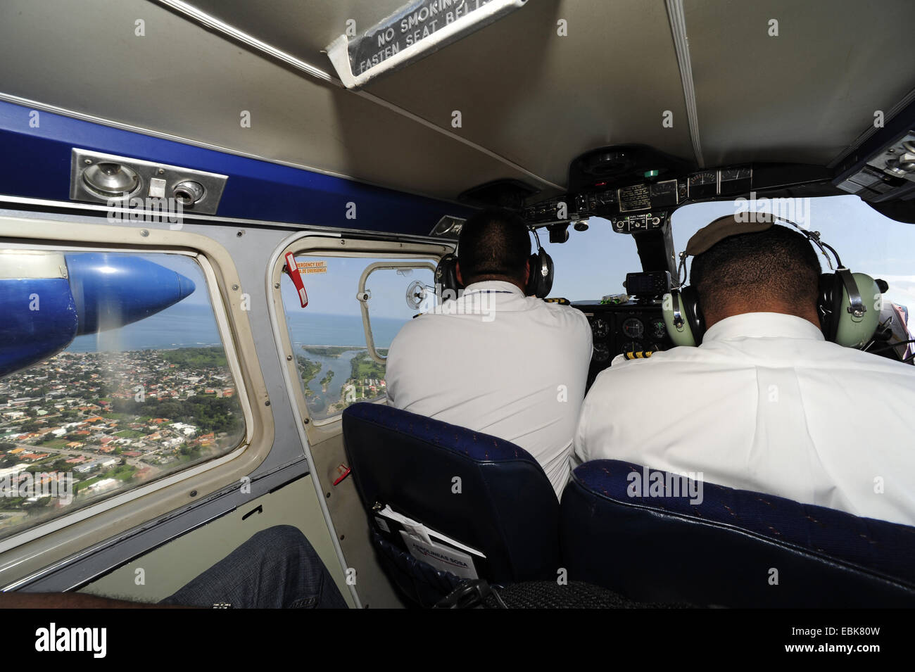 Vista sobre los hombros de los dos pilotos de un avión de hélice Atlantik volando a lo largo de la costa, Honduras Foto de stock