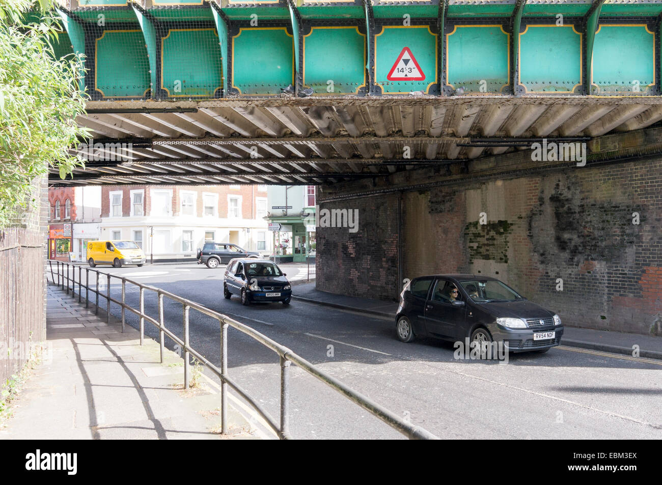 Automóviles circulando bajo el puente de hierro con aviso de limitación de altura Foto de stock