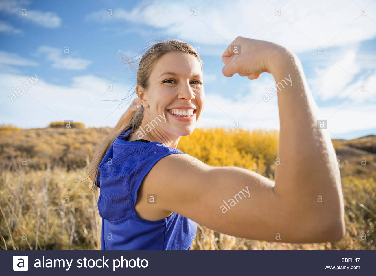 Mujer entusiasta flexionando los músculos en el soleado campo rural Foto de stock