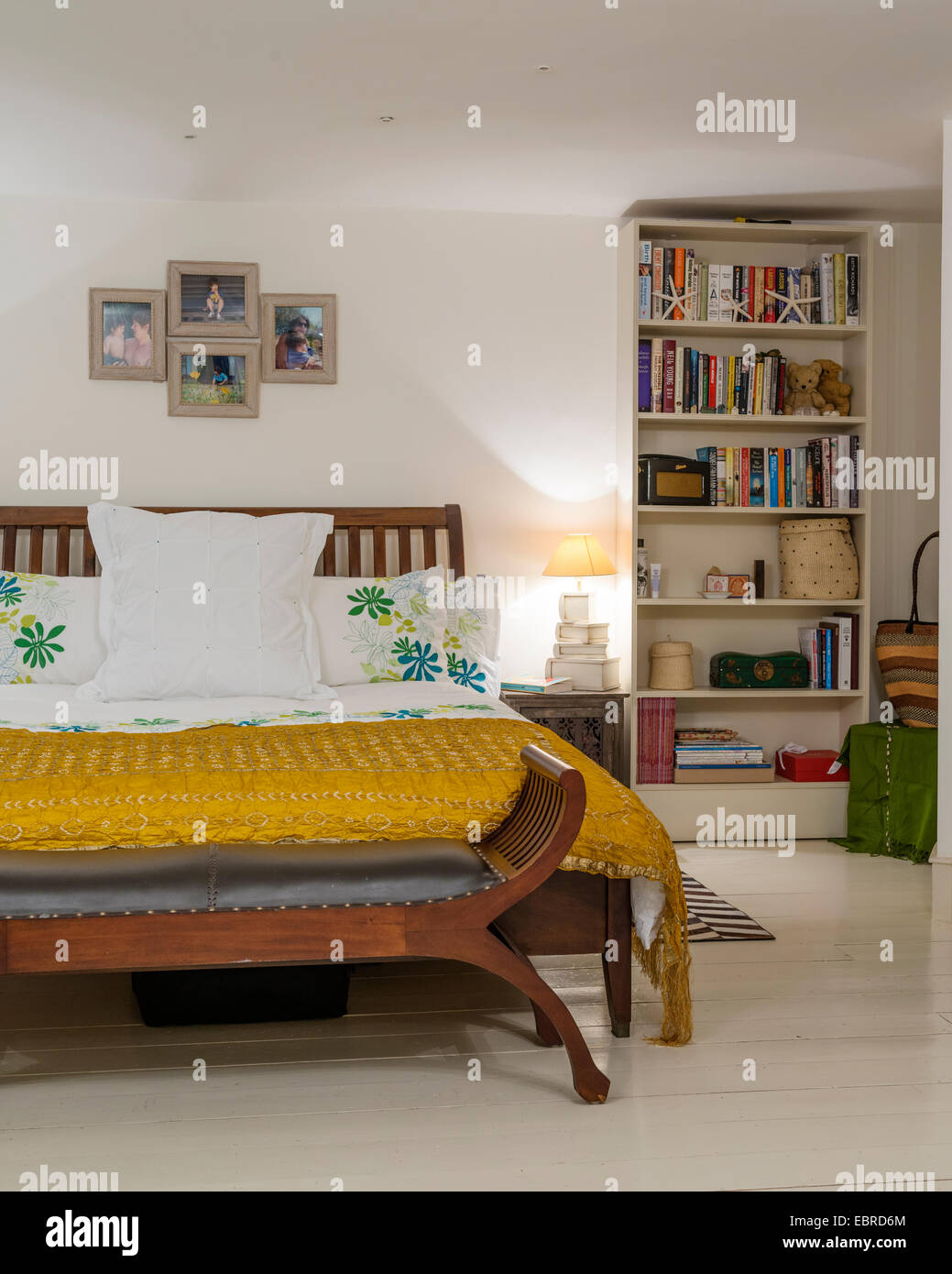Dormitorio con cama de seda amarilla cubierta y estantería Foto de stock