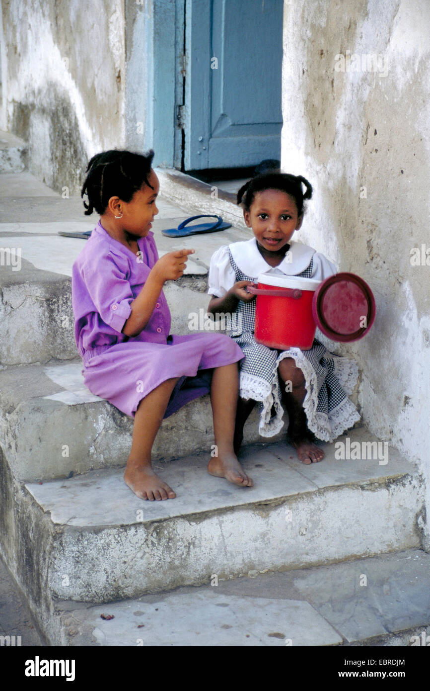 Dos pequeñas muchachas africanas sentados juntos en una escalera exterior y chatear, Tanzania Foto de stock