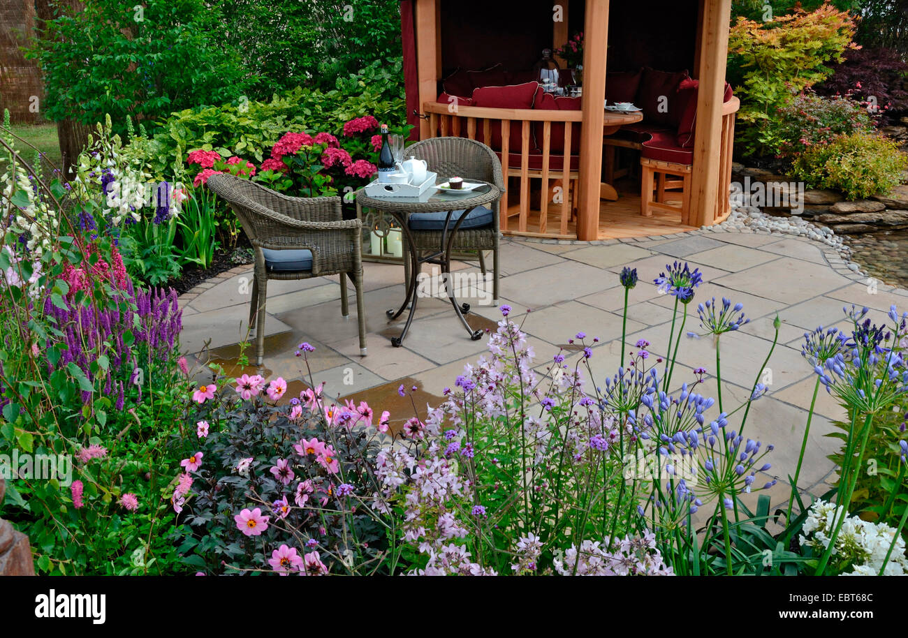 El área del patio en un jardín acuático reflectante con borde de flores coloridas y asientos Foto de stock