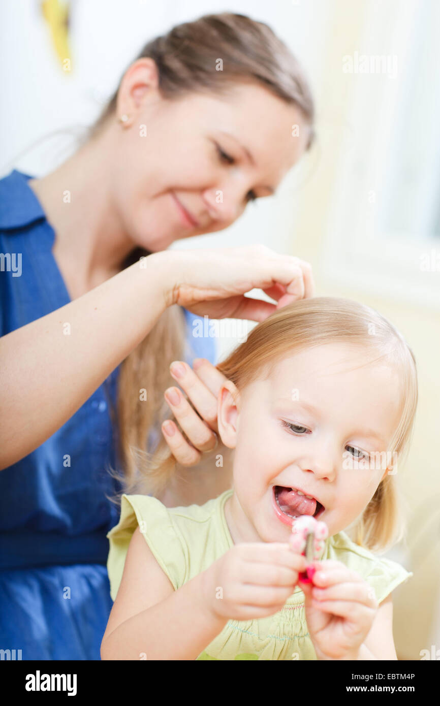 La joven madre poniendo en trenzas a su pequeña hija Foto de stock