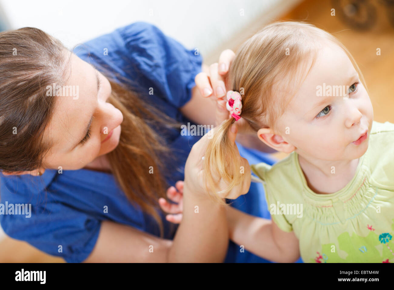 La joven madre poniendo en trenzas a su pequeña hija Foto de stock