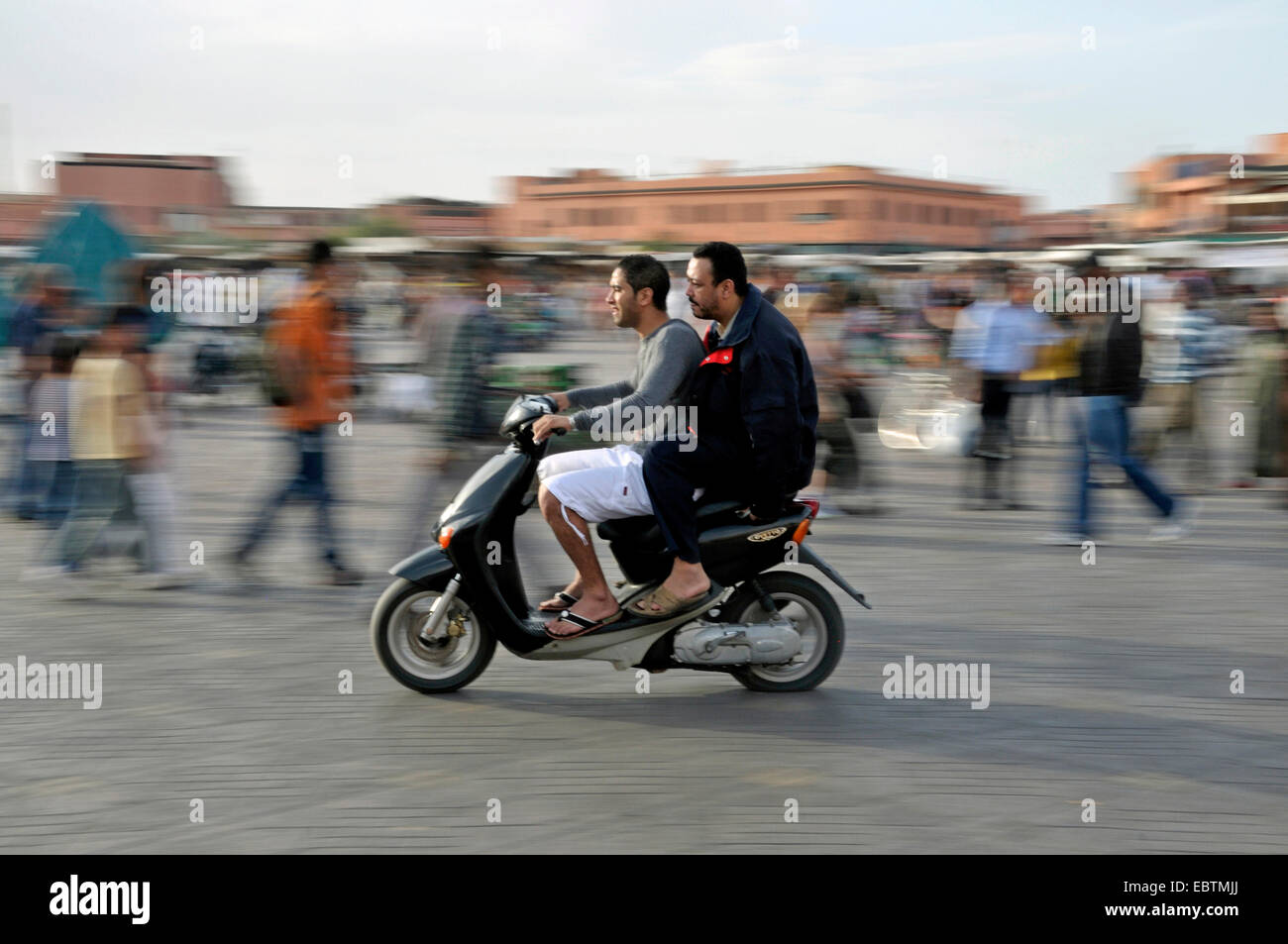 Dos Marroquíes en un motor-scooter cruzando Djemaa El Fna , Marruecos, Marrakech, Medina, Djemaa El Fna. Foto de stock