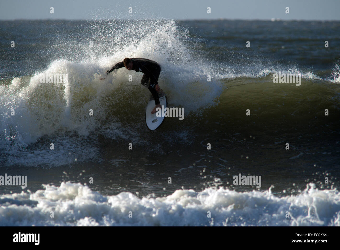 Un surfista rodeado en spray se convierte en la cima de una ola verde en Gower en Gales. Foto de stock