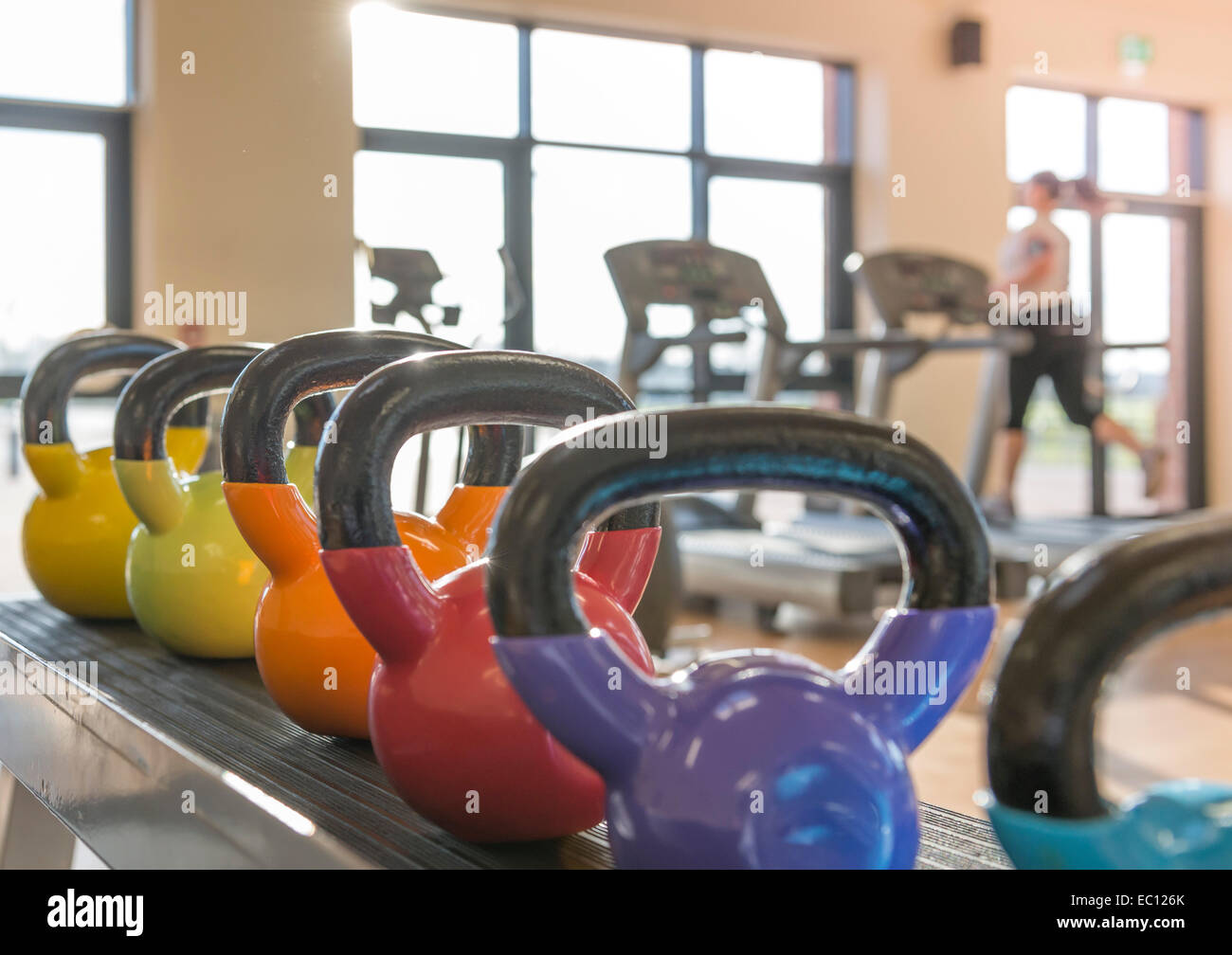 Hervidora de pesas en el gimnasio con una mujer en una cinta en un gimnasio Foto de stock