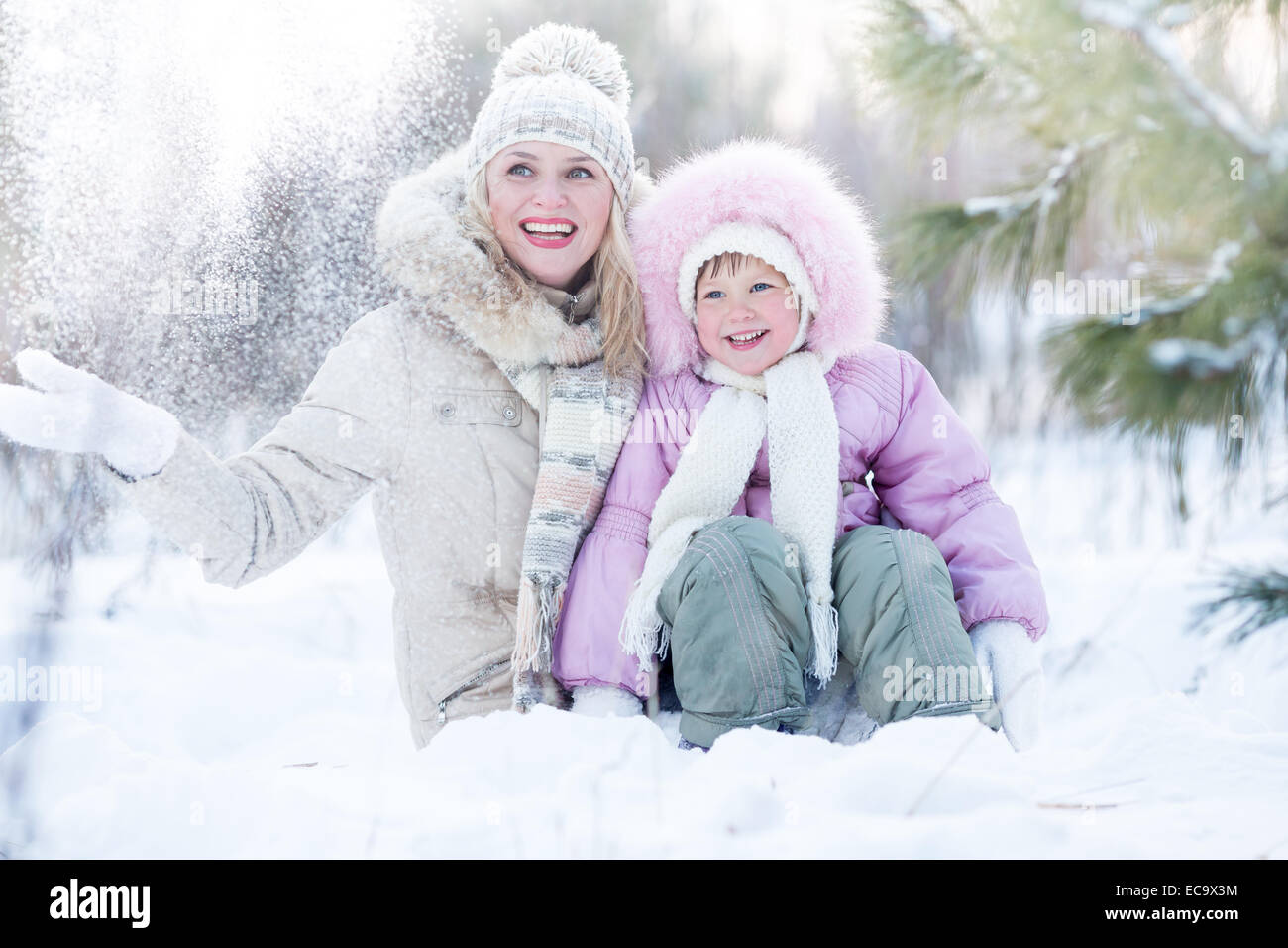 Familia feliz madre e hija sentados en la nieve de invierno al aire libre Foto de stock
