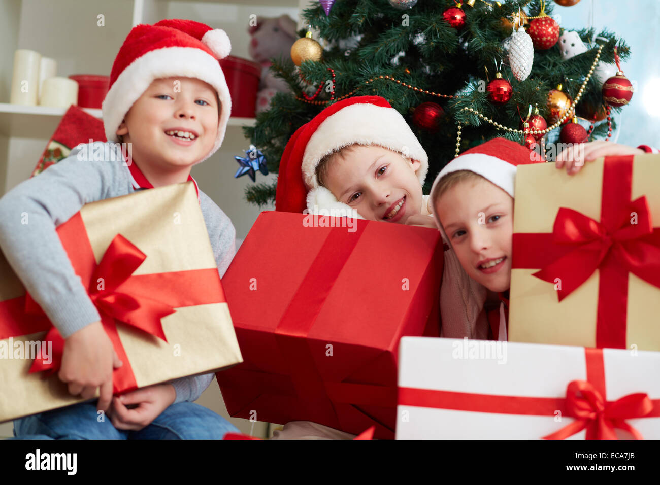 Tres chicos en Santa celebración gran giftboxes caps Foto de stock