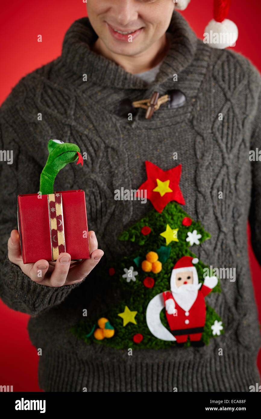 Hombre en tejido sweater mostrando juguete serpiente en giftbox abierto Foto de stock
