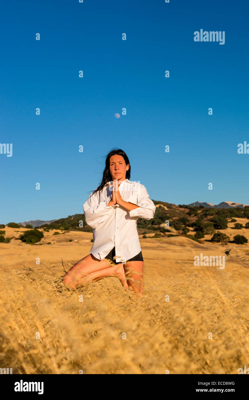 Una mujer en una pose de yoga en un campo de hierba dorada Foto de stock