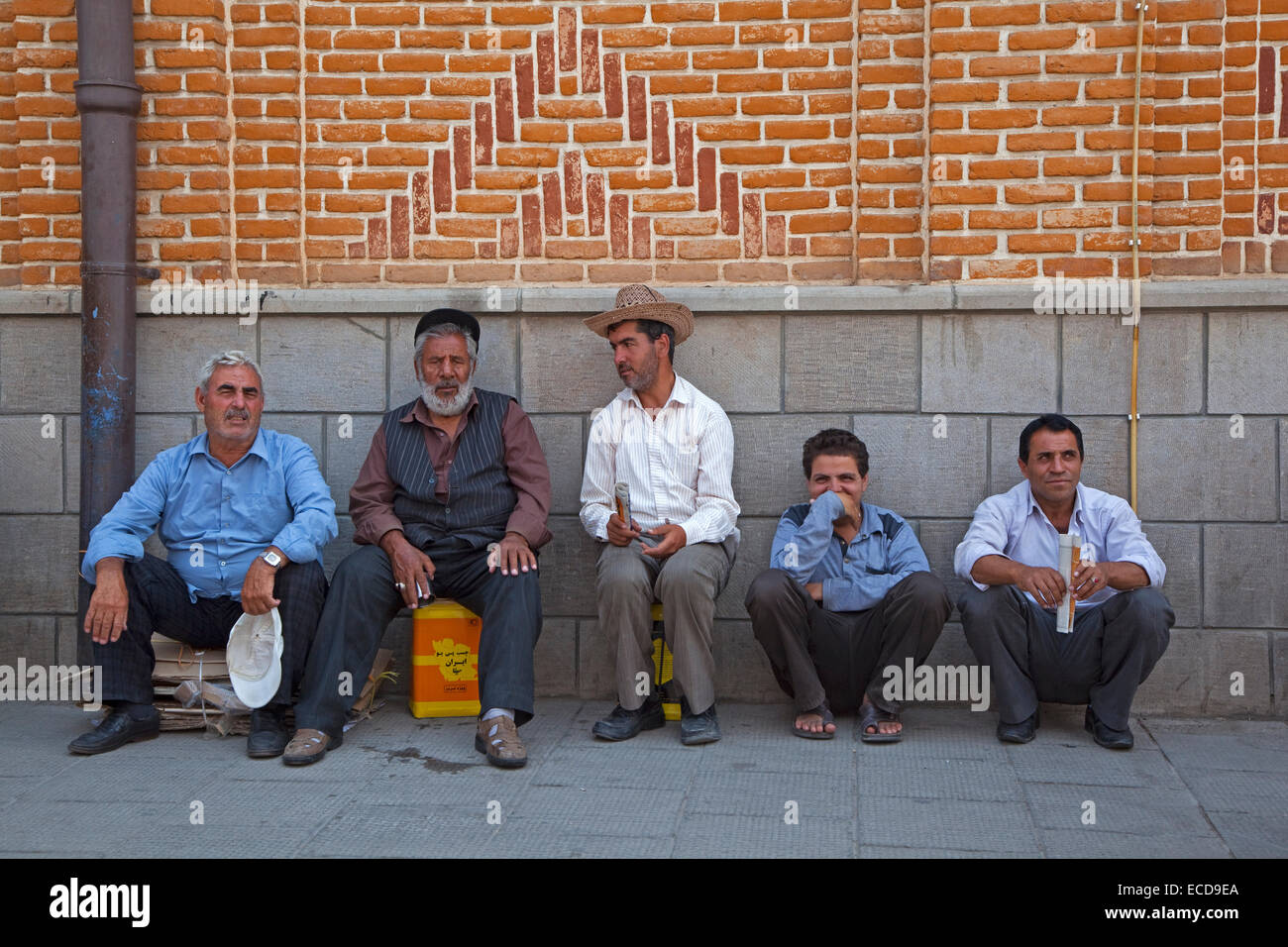 Grupo de hombres iraníes apoyado contra la pared en la calle en la ciudad de Tabriz, Irán, Azerbaiyán Oriental Foto de stock